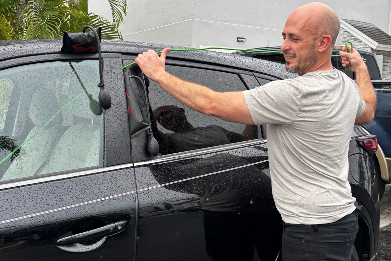 Oscar, A&O Premium Locksmith technician, unlocking a car door on a Miami driveway using a professional air wedge and long-reach tool